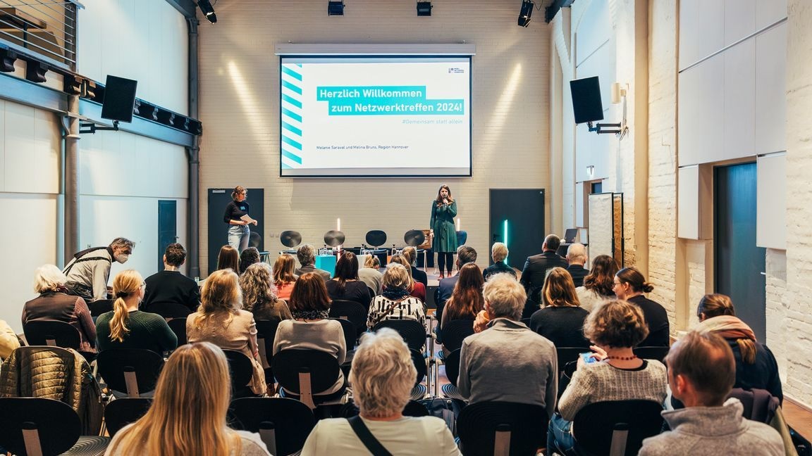 Eine Frau steht auf einer Bühne und spricht zu einer Gruppe von Menschen